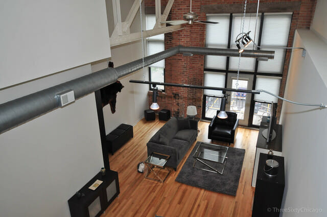 Photo of two story West Loop loft interior living space in Beacon Lofts - huge wall of windows at the end, black and grey modern furniture against white walls and exposed brick.