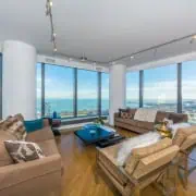 Interior of a luxury Chicago condo showing an open concept living room and kitchen with floor-to-ceiling windows overlooking the downtown city skyline.